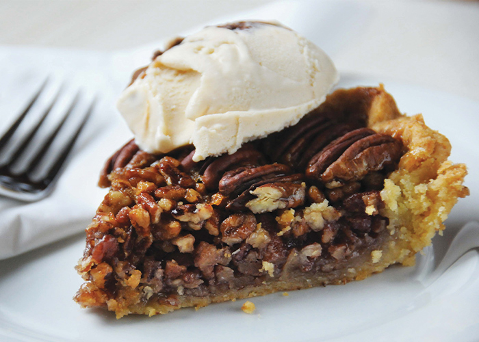 Pecan pie with chocolate filling, topped with a scoop of vanilla ice cream.