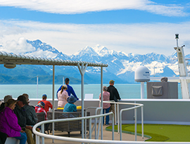 Guests enjoying snow-capped Alaska mountain views from a cruise ship deck