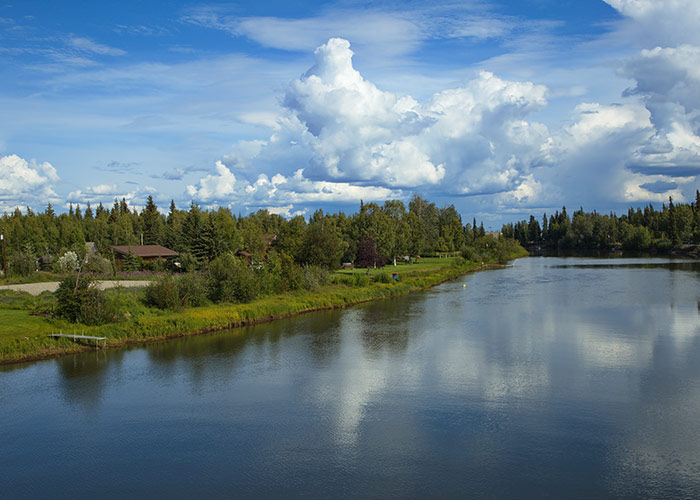 The Chena River, bordered by lush greenery, and a cloudy sky.