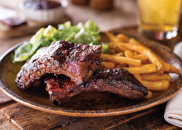A plate of southern barbecue food, with pork ribs and shoulders, french fries, and a salad.