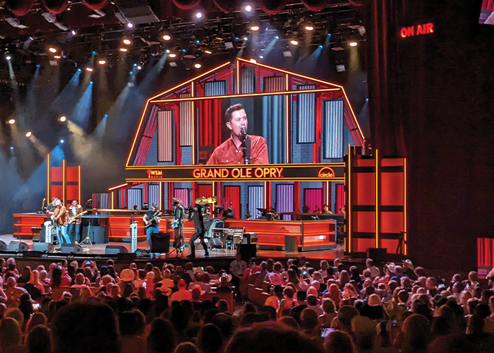A live concert at the Grand Ole Opry in Nashville, where a male singer and his band performs in front of a large crowd of hundreds of people.