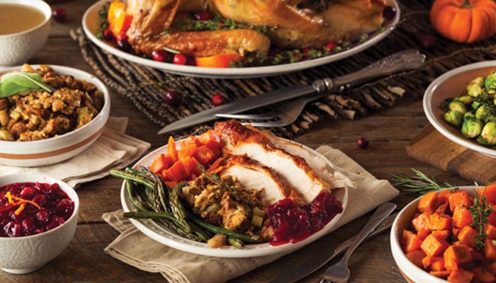 A table with Thanksgiving dishes: turkey, stuffing, cranberry sauce, sweet potatoes, and Brussels sprouts.