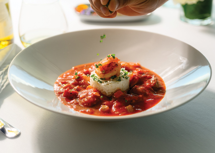 A large bowl of jambalaya, a blend of rice, meat, seafood, vegetables, and spices, in the center of a red sauce.