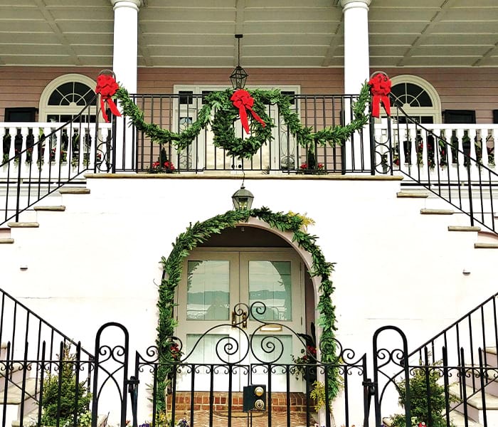 A historic Southern mansion decorated with holiday garlands and bows.