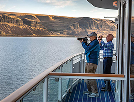 Two American Cruise Lines cruise guests taking photos of the scenic desert canyon mountain views from the deck of an American Riverboat