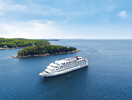 White American Cruise Lines ship sails near a green island on calm blue water under a clear sky.