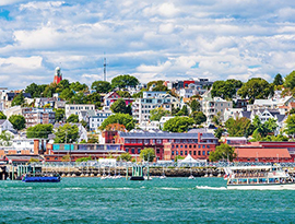 Small cruise ship near colorful waterfront town, passengers on deck, scenic US river cruise.