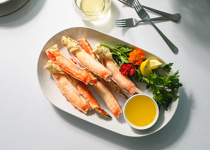 Plate of Alaskan-inspired cuisine, featuring crab legs with lemon, herbs, flowers, and butter sauce.